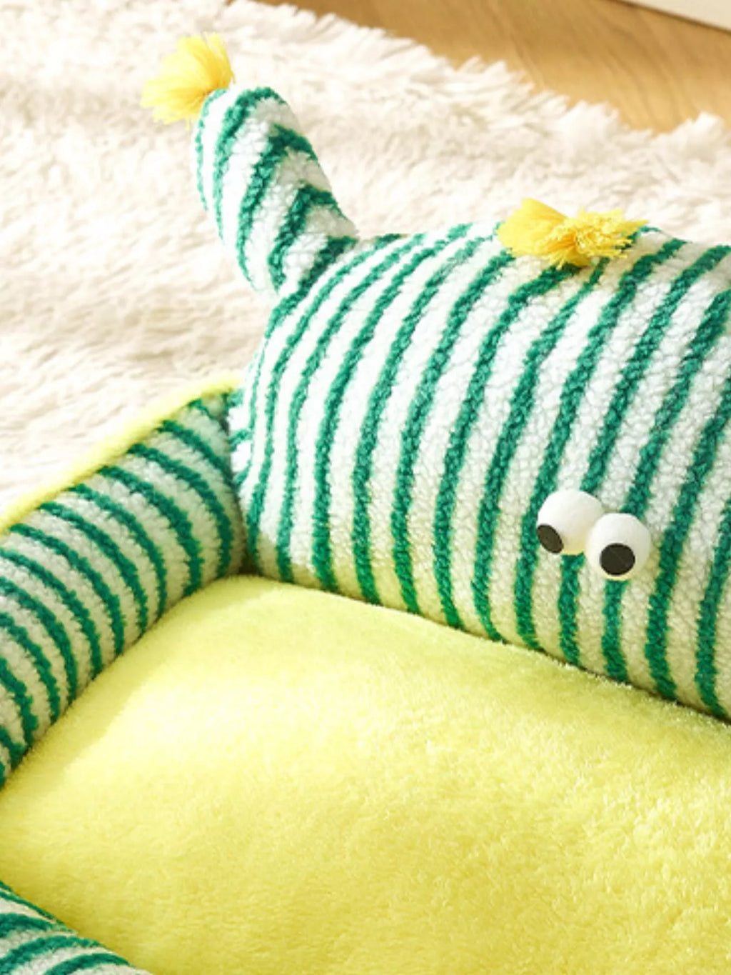 Green and white striped toy with googly eyes on a yellow surface